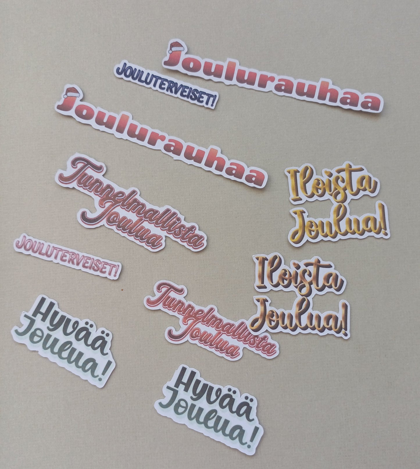 Erilaisia joulutervehdyksiä, kuten joulurauhaa, jouluterveiset, hyvää joulua, iloista joulua. Eri värejä. Yhteensä 10 kappaletta.