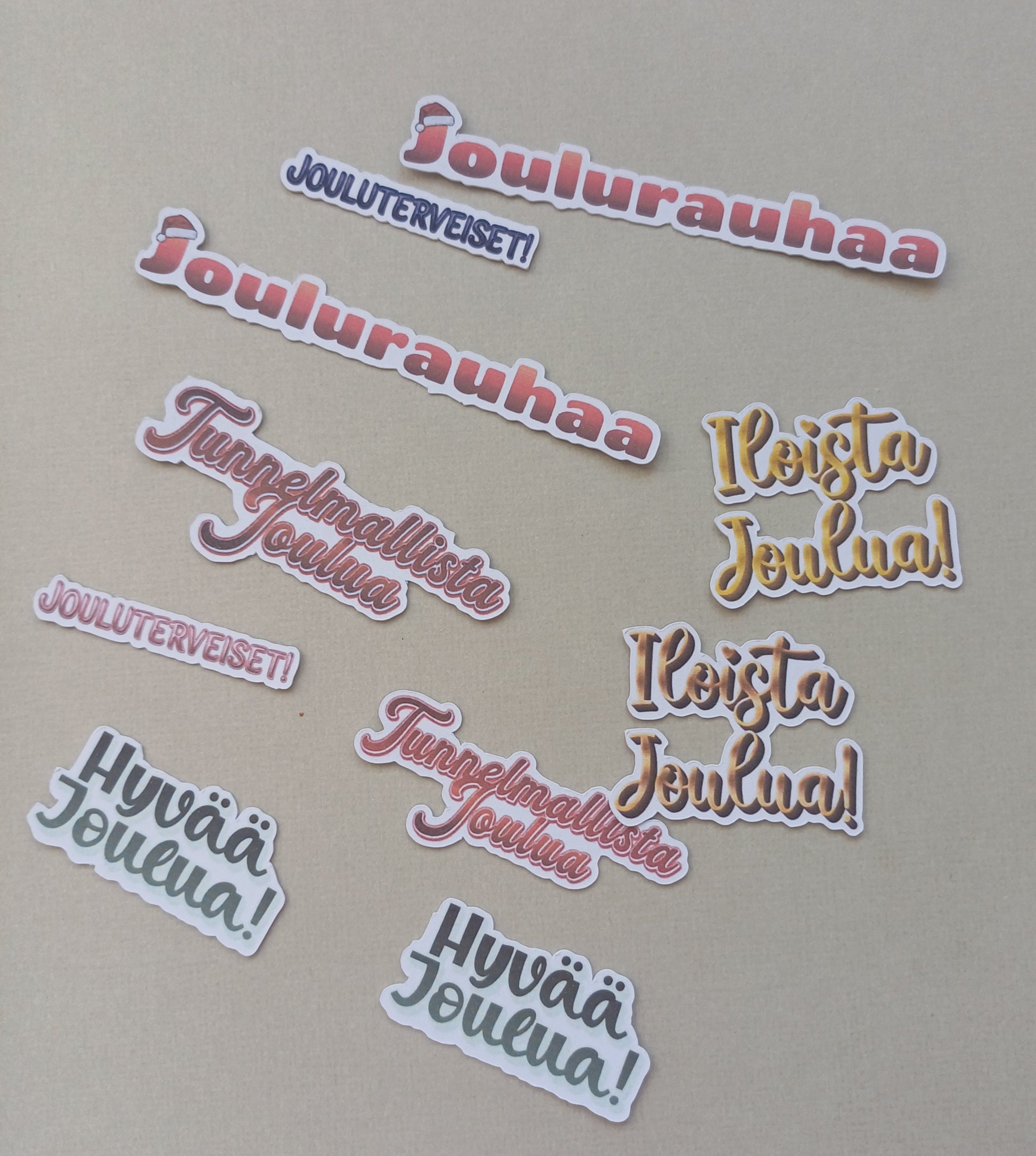 Erilaisia joulutervehdyksiä, kuten joulurauhaa, jouluterveiset, hyvää joulua, iloista joulua. Eri värejä. Yhteensä 10 kappaletta.