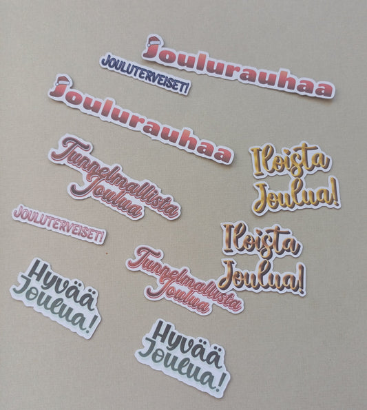 Erilaisia joulutervehdyksiä, kuten joulurauhaa, jouluterveiset, hyvää joulua, iloista joulua. Eri värejä. Yhteensä 10 kappaletta.